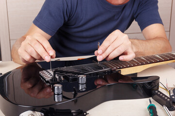 Guitar technician adjusts tremolo bridge on modern electric guitar.