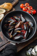 Delicious cooked seafood mussels with tomato sauce, on frying iron pan, on black wooden table background