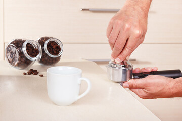 Coffeemaker hands presses coffee tablet in holder with tamper on table.