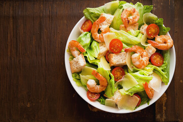 Caesar salad with shrimp, croutons and parmesan on an old rustic table, top view