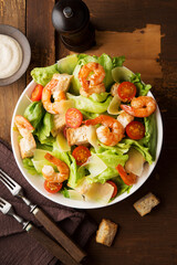 Caesar salad with shrimp, croutons and parmesan on an old rustic table