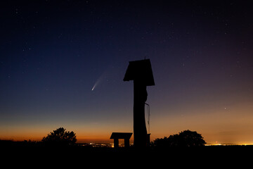 Wooden curfew bell tower on the hill with the comet Neowise, stars and the city on the background...