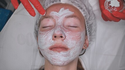 Application of a cream mask on the face of a girl with problem skin in the salon.