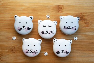 Cute macarons in a shape of cats on wooden board, small sugar snowflakes around, top view. Christmas or winter time. Creative baking