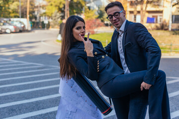 Naklejka premium Two suited colleagues posing for the camera. The male colleague is holding the waist and the leg of the female