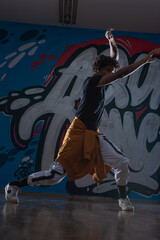 Young black male dancing hip hop style in an urban setting. he is wearing a orange outfit and is on a graffiti background.