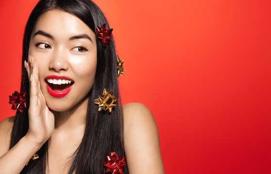 Image of beautiful asian fashion girl with holiday christmas gift wrap on hair, smiling and looking surprised at copy space, advertising beauty product on winter holidays, new year 2022 concept