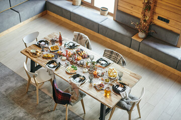 Several chairs around large wooden dining table served with homemade food for festive dinner in...