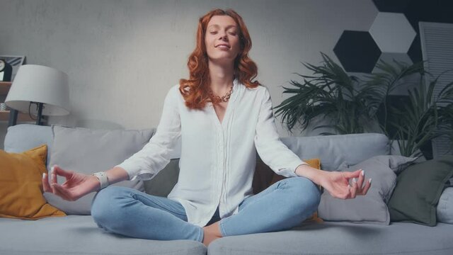 Happy Red Haired Woman Sit Cross Legged On Comfy Sofa In Living Room Closed Eyes Do Meditation Practice Feels Inner Harmony And Balance, Improve Self-conscious, Mindfulness State, No Stress Concept.