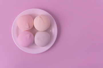 Marshmallow of delicate shades lies on a white teatka. Pink background, top view. There is room for text