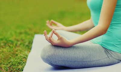 Young woman doing yoga exercises on a mat on the grass in summer park