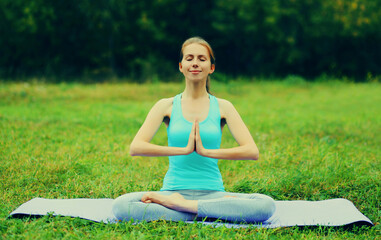 Young woman doing yoga exercises on a mat on the grass in summer park