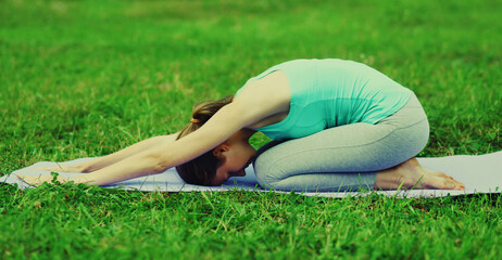 Fitness woman doing yoga exercises back stretching on a mat on the grass in summer park