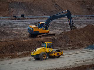 Road roller and excavator on the construction of a new road. Highway construction site details