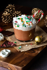 A cup of hot chocolate with whip cream and sprinkles, served with a candy cane.