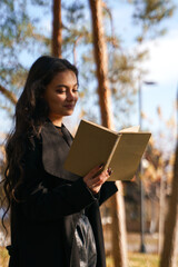 Fototapeta premium A girl in a black coat walks in the park with a book in her hands