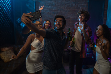Diverse group of young people dancing at the night club, and taking a selfie with smartphone