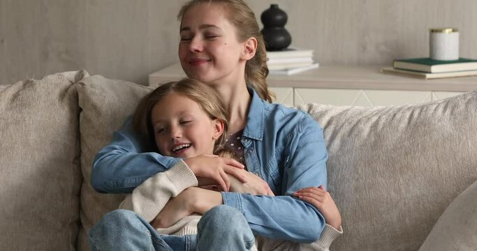 I love you so much. Tender young mother sit on couch hold little preteen child girl in arms talking laughing enjoying pastime together. Happy small daughter feel safe protected in caring mom embraces