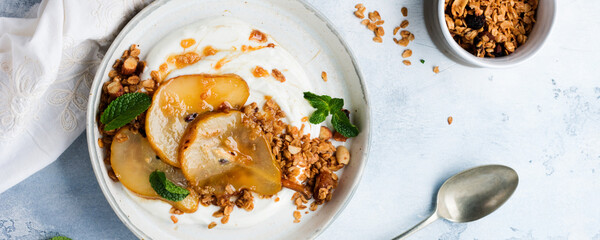 Greek yogurt with caramelized pear, granola, nuts and melted sugar for a wholesome breakfast on a gray ceramic plate. Rustic style. Top view