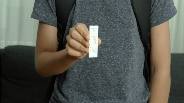 Coronavirus pandemic protection. Teenager using rapid antigen test kit for self test covid-19 epidemic at home. Boy with backpack looking at test and showing negative results on test strip