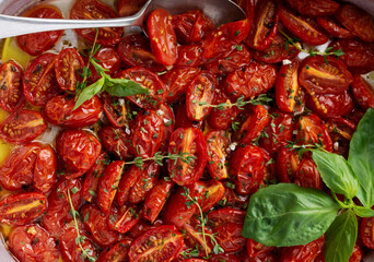 Baked cherry tomato with garlic, thyme and basil in old baking pan on concrete vintage background. Top view