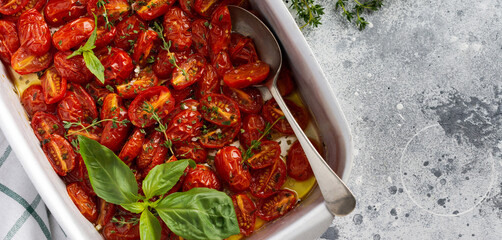 Baked cherry tomato with garlic, thyme and basil in old baking pan on concrete vintage background. Top view