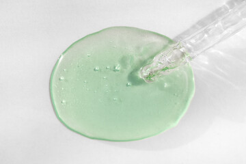 Pipette with green hyaluronic acid on white background. Cosmetics and healthcare concept closeup. Dose of serum or retinol with air bubbles. Top view. Luxury gel or beauty product presentation, macro