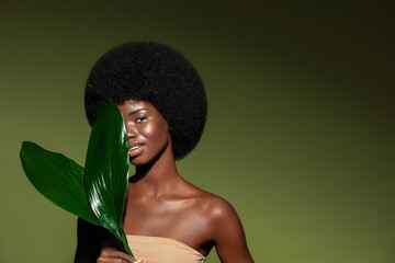 Natural organic cosmetics concept.  Beauty portrait of young beautiful african american woman with posing with exotic leaves, curly afro hair against green exotixc plants background.