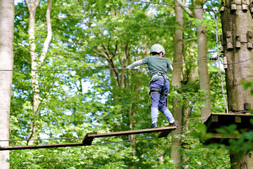 School boy in forest adventure park. Acitve child, kid in helmet climbs on high rope trail. Agility...