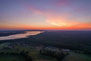 Panorama of the small village. Aerial landscape of the lake surrounded by the lush forest. Blue sky and pastel clouds.