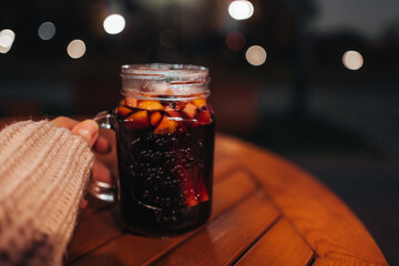 Woman's hand in a cozy sweater holding a glass of hot fruit red wine