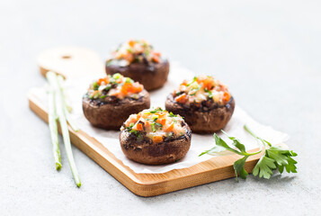 Mushroom appetizer, Stuffed royal champignons with ham, cheese, tomato and parsley on a wooden board on a light gray background