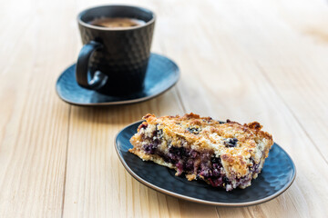 Homemade delicious sliced Apple Blueberry Pie on a black serving plate and a cup of black coffee on a wooden table. Selective Focus