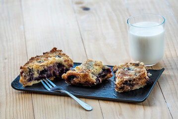 Homemade delicious sliced Apple Blueberry Pie on a black serving plate on a wooden table with a glass of milk