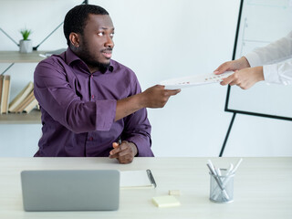 Office work. Colleagues cooperation. Do task. Male worker taking documents from woman sitting workplace in light room interior.