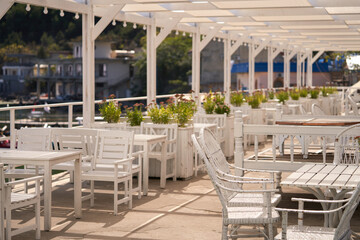 Outdoor cafe with white wooden furniture on the seashore. The cafe is decorated with planters with...