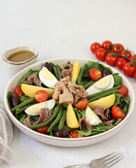 Traditional French salad nicoise: with tomatoes, tuna, olives, eggs, green beans and anchovies on a white plate. Green salad with tuna, eggs, olives, tomatoes.