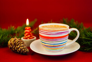 Scena natalizia con una tazza di caffè colorata e con una pigna accanto e una candela rossa accesa...