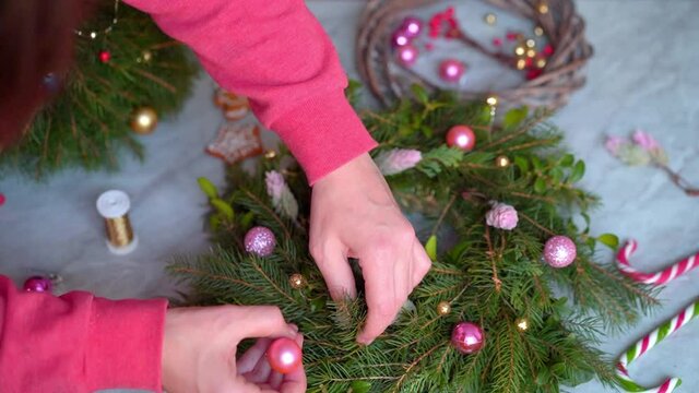 Making rustic christmas wreath. Hands decorate a Christmas wreath with pink round toys. Close-up. Making crafts. Seasonal holiday workshop online, making festive decorations at home. Selected focus.