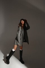Fashion model girl in a fashionable oversized blazer, bra and fashionable boots over gray background