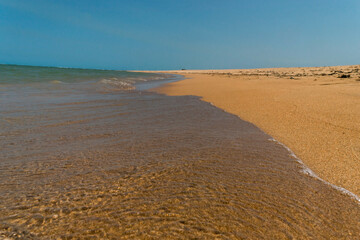 praia deserta com areias escuras e céu azul