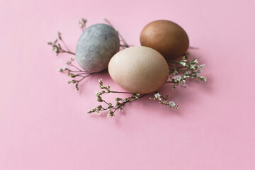 Stylish easter eggs and flowers on pink background. Modern natural dyed easter eggs and flowers border. Greeting card template, easter background. Space for text. Happy Easter!