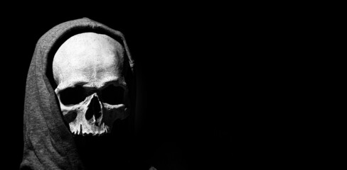 Human skull in hood close up on black background. Free space - obrazy, fototapety, plakaty