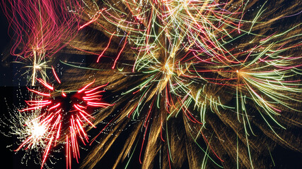 Multiple bursts of colorful fireworks arching across a black sky