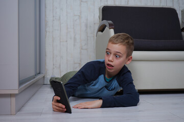 młody chłopak leży na podłodze patrzy w telefon, jest zdziwiony