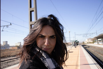 young brunette woman next to railroad arden with luggage, waiting for passenger train.