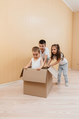 Fototapeta na wymiar A friendly family of children boys and girls play and roll around each other in a cardboard box, rejoice at moving to a new apartment against the background of cardboard boxes.Transportation of goods.