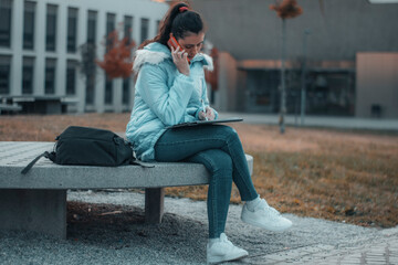 Chica joven de pelo castaño con mascarilla llamando por su telefono movil mientras revisa los...