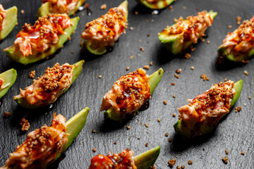 Sliced avocado seasoned with sauce lies on a dark background. Selective focus.