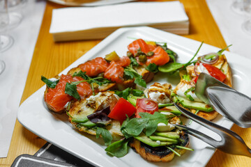 Canapes with red fish, mozzarella, tomatoes and herbs are on a plate.